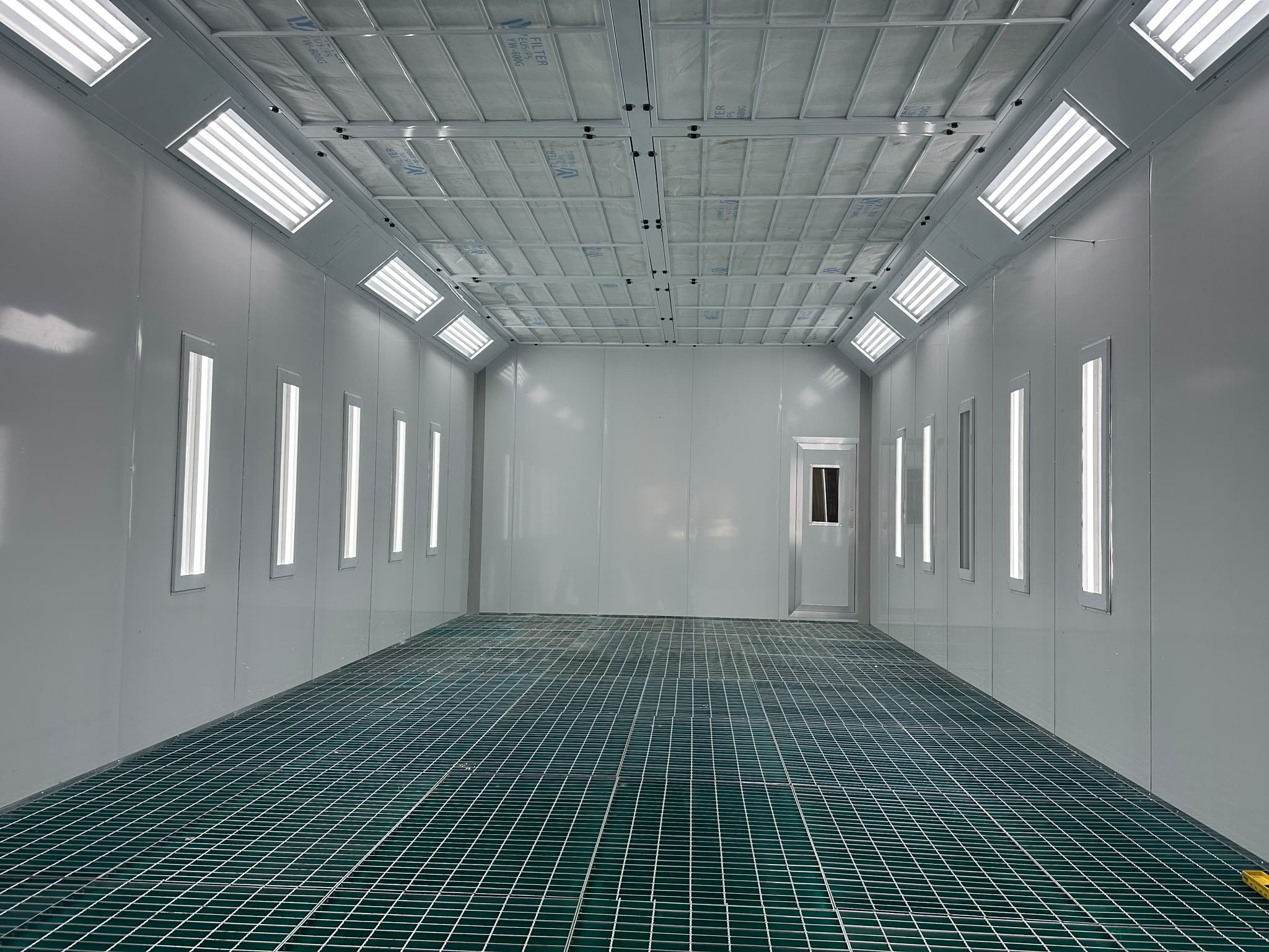 Interior of a freshly installed spray booth with bright lighting and a steel grated floor
