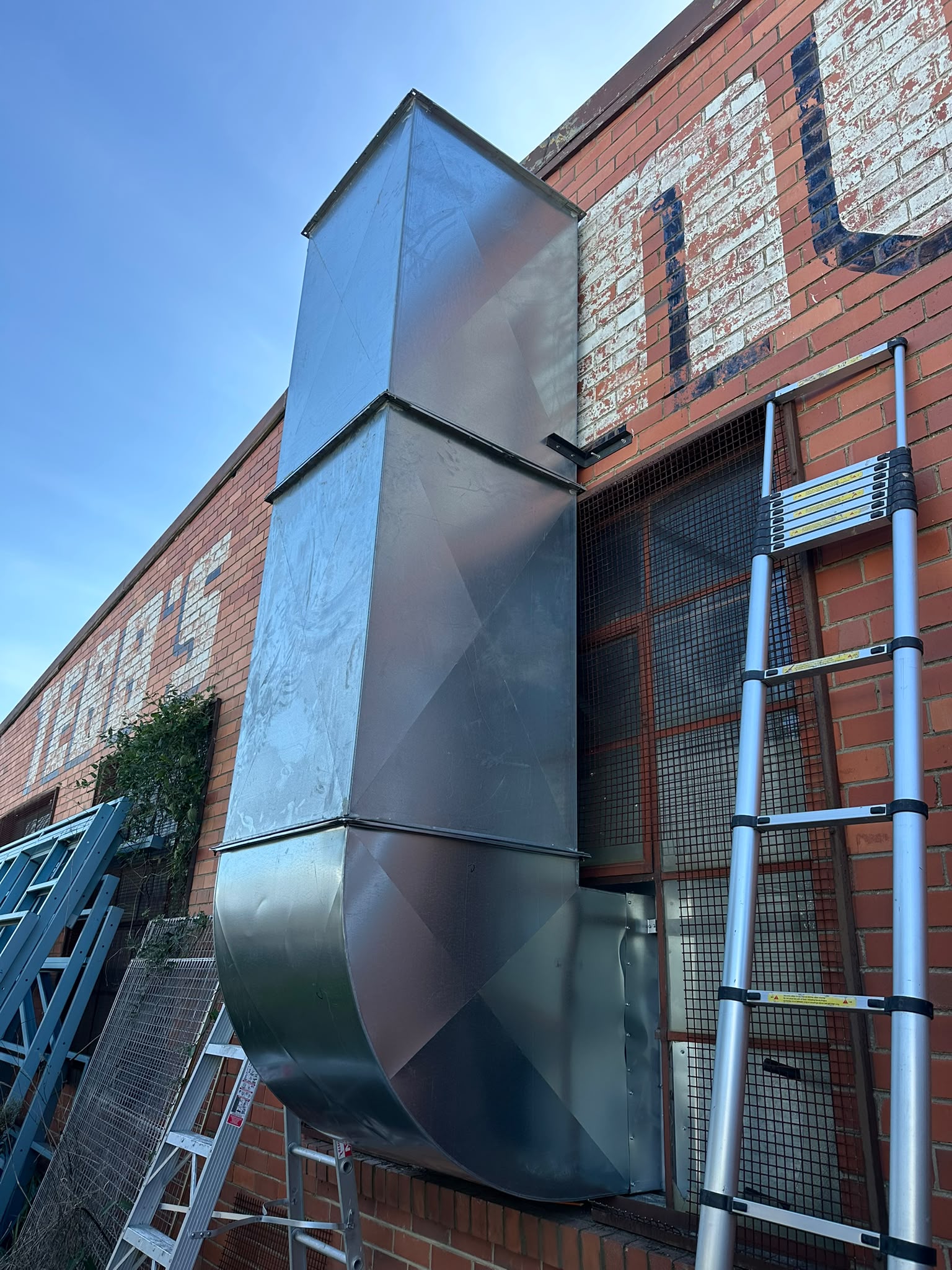 Galvanised steel extraction ducting installed on the exterior brick wall of a building